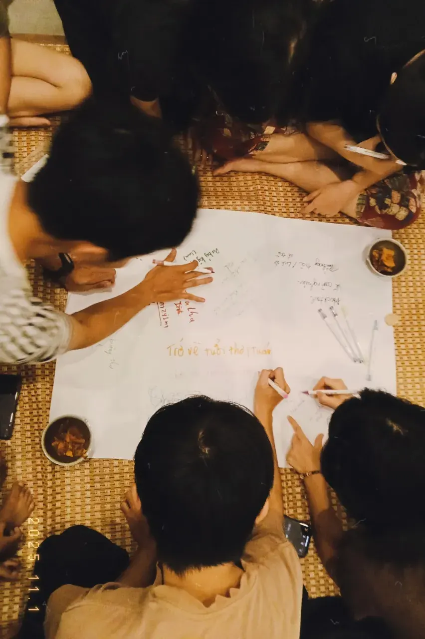 Mọi người cùng ngồi vẽ và viết trên một tờ giấy lớn trải trên chiếu.